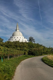 White pagoda surrounded by green nature and meadows under a blue sky, Stupa am Wagram Grafenwörth
