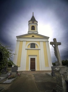Yellow church with tower and cross in a cemetery under a cloudy sky, Kammersdorf Hollabrunn