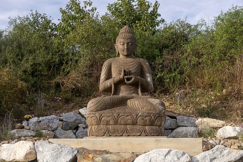Sitting Buddha statue surrounded by stones and vegetation, Stupa am Wagram Grafenwörth Weinviertel