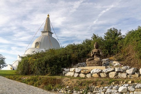Buddha statue sitting on stones next to a pagoda in a green landscape, Stupa am Wagram Grafenwörth