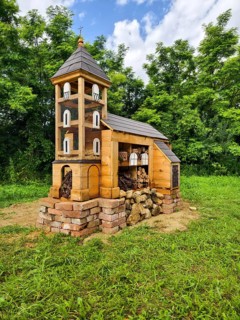 Miniature church made of wood Insect hotel surrounded by green landscape under a cloudy sky,