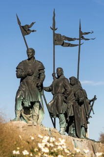 Bronze warrior statues with flags, conveying a historic and majestic feeling, stand against a blue