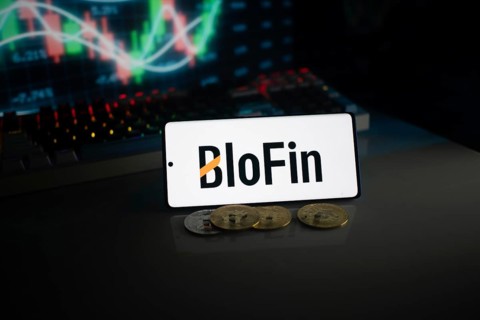 BloFin display with coins in front of an active stock chart under neon lighting