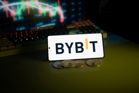 Bybit logo displayed on a phone, foregrounding trading charts and coins