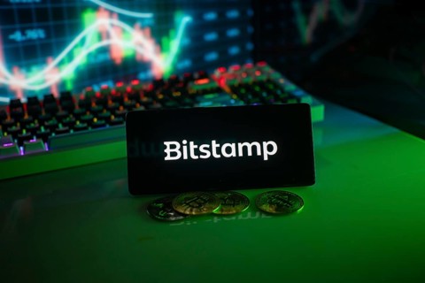 Bitstamp logo in a dim setting with coins and a vivid chart