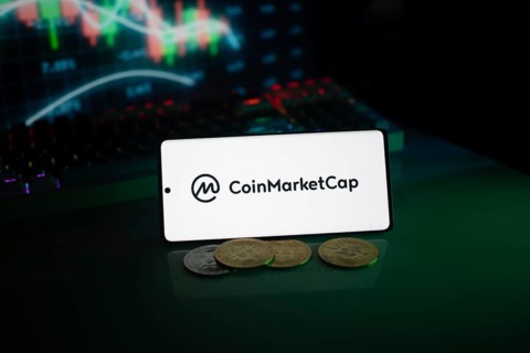 CoinMarketCap logo in a dark environment highlighted by coins and a glowing chart