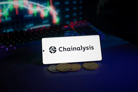 Chainalysis logo on phone, accompanied by coins and stock chart, highlighting digital finance