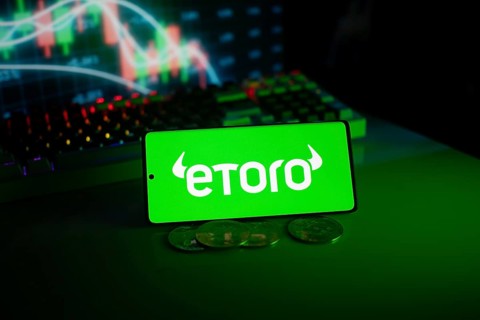EToro logo on phone with coins and stock chart backdrop, evoking digital trading atmosphere