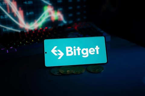 Bitget logo on smartphone with coins and stock chart, highlighting finance and trading theme