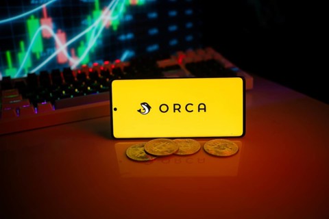 Yellow Orca logo on phone with coins and market screen, indicating crypto trading