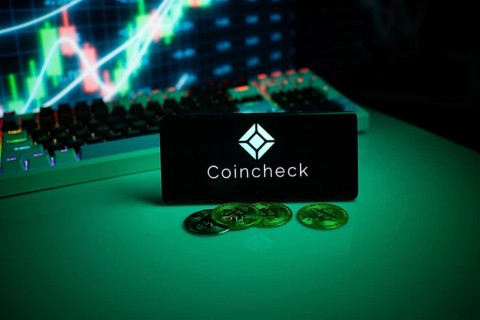 Coincheck on a smartphone with coins and stock market data in the background