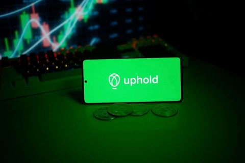 Uphold on a smartphone with coins and vivid stock market charts visible