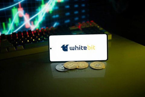 Whitebit displayed on a smartphone with coins and financial market visuals