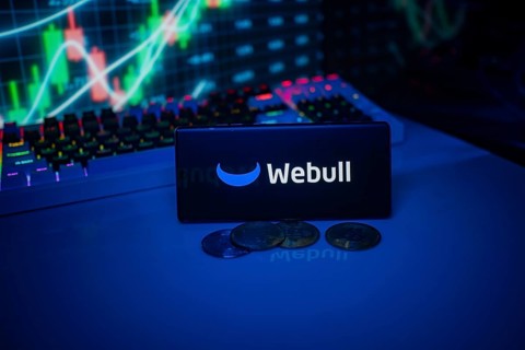 Webull depicted on a smartphone with coins and stock market indicators