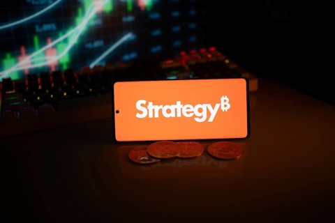 Phone shows Strategy logo with Bitcoin symbol and crypto coins on vivid screen