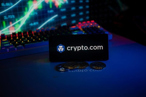 Phone displays Crypto.com logo with crypto coins and vibrant trading screen