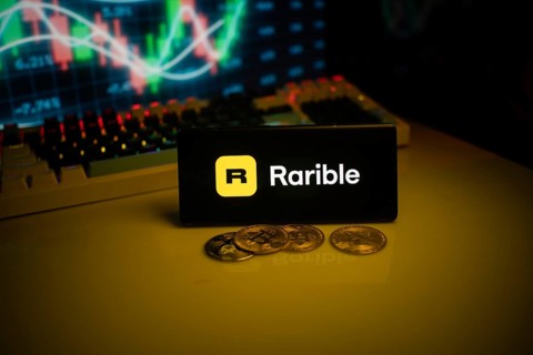 Phone displays Rarible logo with crypto coins and trading graph in background