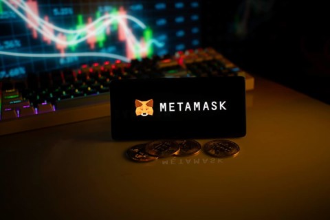 Phone features MetaMask logo with crypto coins and brightly lit trading screen