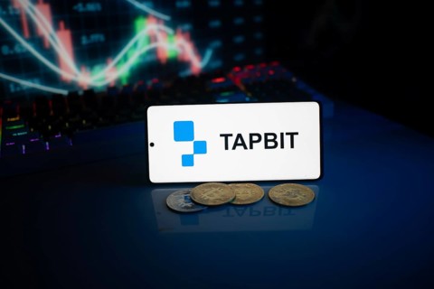 TAPBIT app on phone with coins and market chart in the background