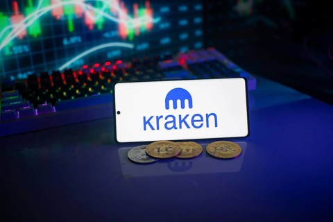 Kraken logo shown on a smartphone with digital currencies and trading charts behind