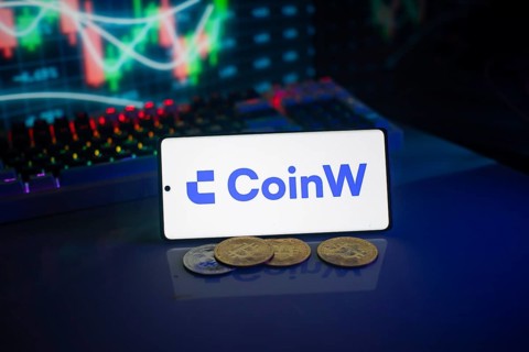Coinw logo on a phone set against a backdrop of digital currencies and trading charts