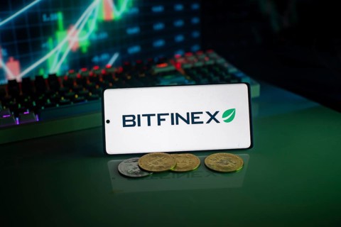Bitfinex logo on a smartphone with cryptocurrencies and financial trading graphs behind