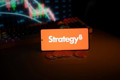 Phone shows Strategy logo with Bitcoin symbol and crypto coins on vivid screen