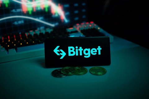 Bitget logo with coins on a desk, set against trading graphs backdrop