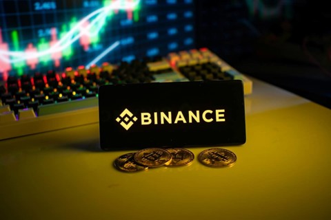 Binance logo on black screen with coins and trading graphs in background