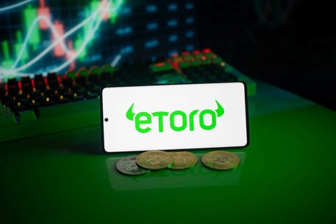 EToro logo on green screen with coins and trading graphs in the background
