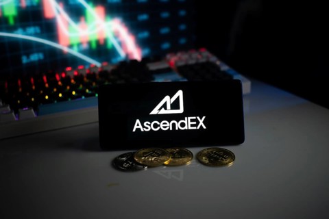 AscendEX logo with cryptocurrency coins on a desk, trading graphs in background