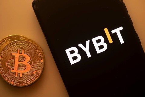 Bybit logo on a black smartphone beside a Bitcoin on an orange background