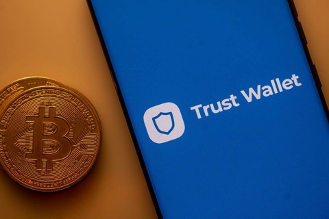 Bitcoin next to a smartphone displaying Trust Wallet app on blue background