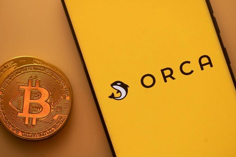 Yellow smartphone screen showing Orca logo with a Bitcoin on an orange background