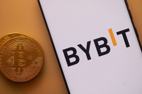 Bitcoin near a smartphone featuring the Bybit logo under orange lighting