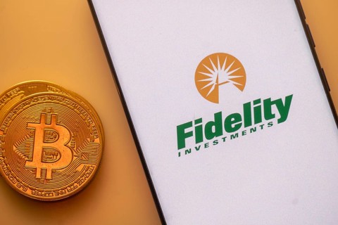 Bitcoin coin next to a smartphone displaying the Fidelity Investments logo on a light background