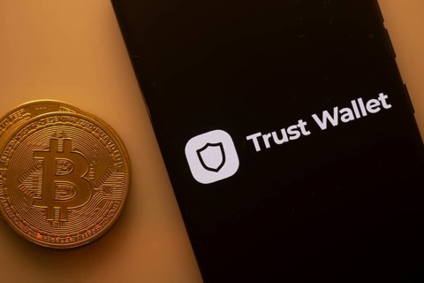 Bitcoin coin near a phone displaying Trust Wallet logo on a black screen
