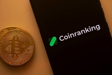 Bitcoin coin beside a phone displaying the Coinranking logo on a black screen