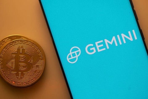 Gemini logo on a smartphone screen alongside a Bitcoin coin