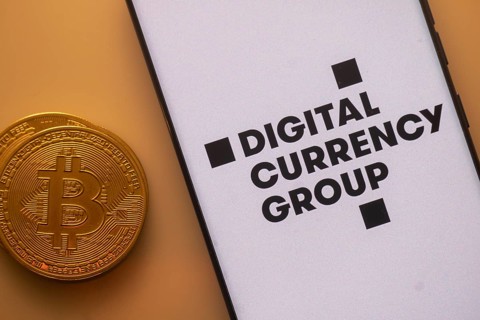 Bitcoin coin next to a smartphone with Digital Currency Group logo on white background