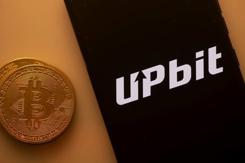 Bitcoin coin beside phone with Upbit logo on black background