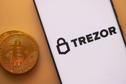 Trezor logo on phone beside Bitcoin, highlighting cryptocurrency security and storage solutions