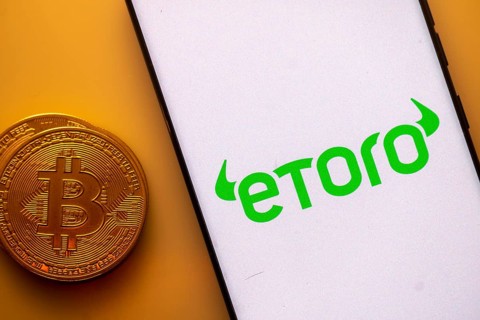 Etoro logo on a smartphone screen next to a Bitcoin coin on an orange background