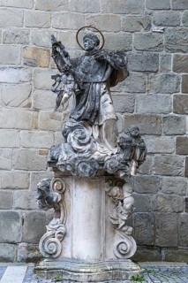 Stone statue of a saint on an ornate pedestal, baroque details in front of a stone wall, parish