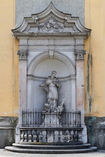 Baroque statue of a saint in a niche on a church wall, surrounded by decorative stone architecture,