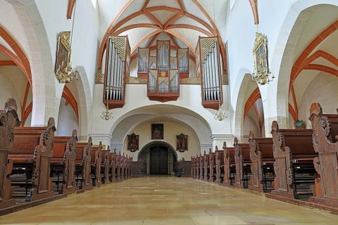 Interior of a church with detailed wooden benches and an impressive organ on the ceiling, St
