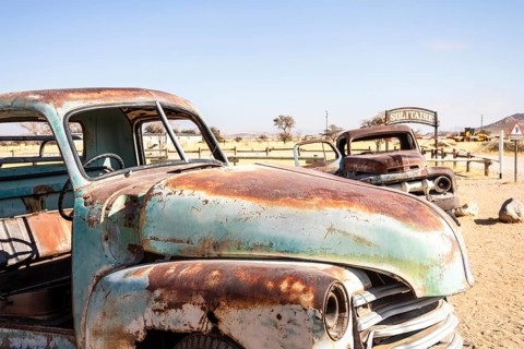 Solitaire's car graveyard in Namibia features rusted vintage cars near small desert buildings, set