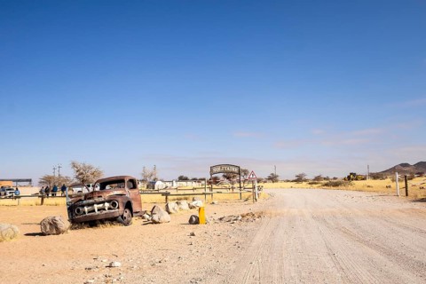 Solitaire's car graveyard in Namibia features rusted vintage cars near small desert buildings, set