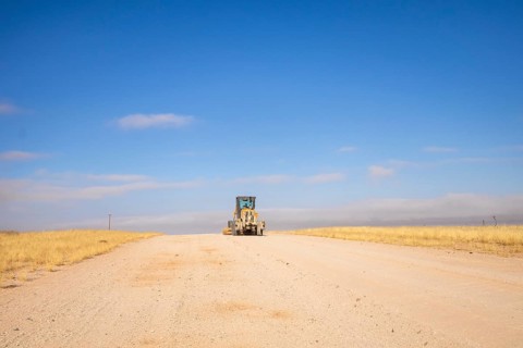 In the remote desert near Solitaire, Namibia, a tractor levels a dirt road across golden sand dunes