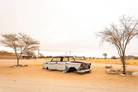 Solitaire's car graveyard in Namibia features rusted vintage cars near small desert buildings, set
